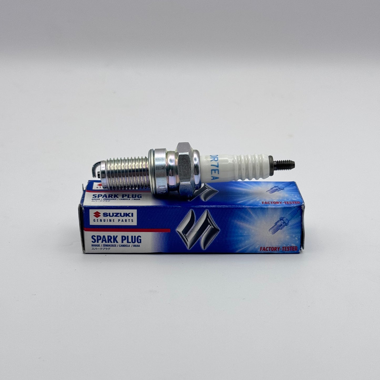 Suzuki spark plug on its packaging against a gray background