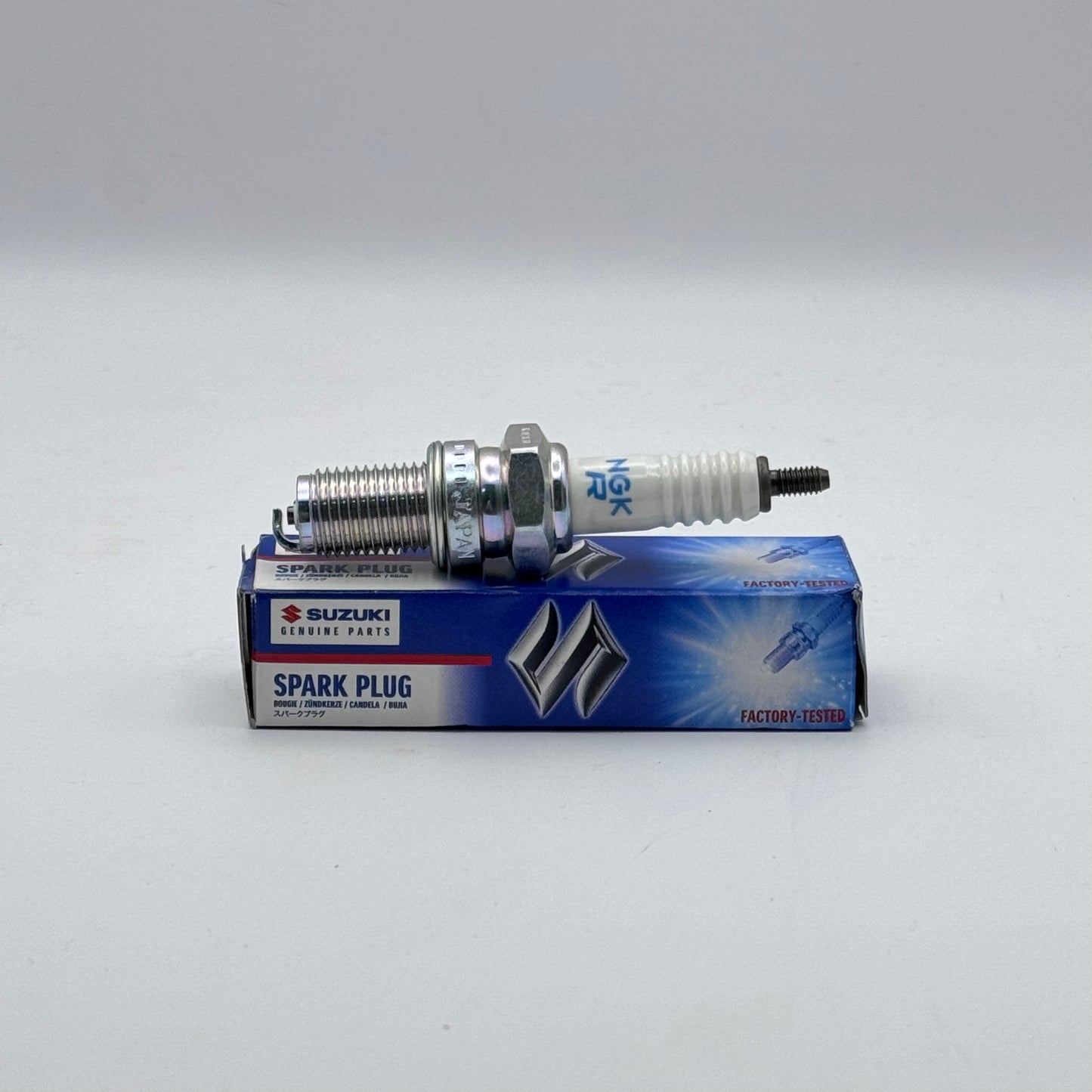 Suzuki spark plug on top of its packaging box against a gray background