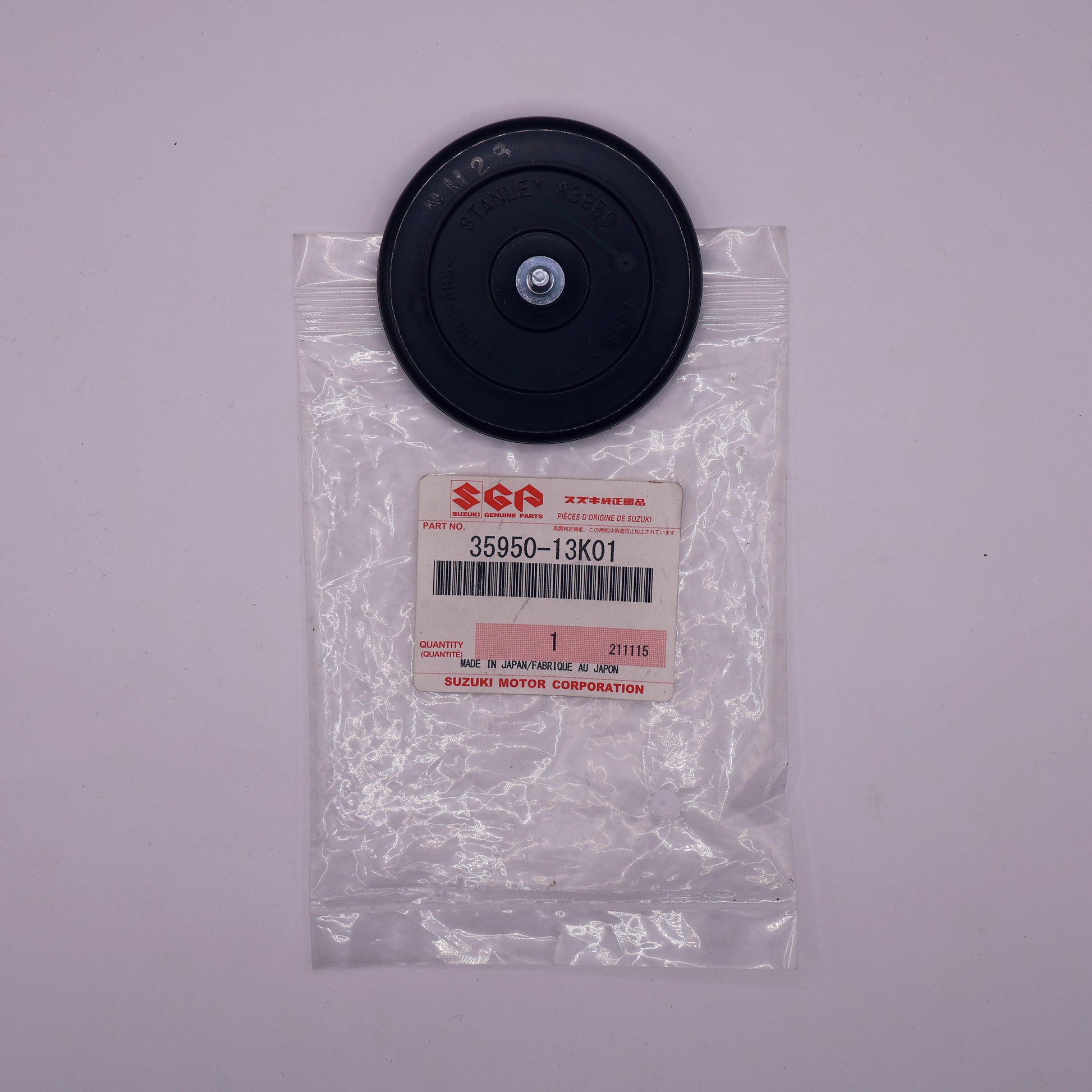 Black circular part in a clear plastic bag with Suzuki label on a gray background
